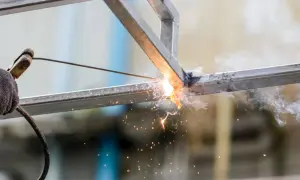 Spawanie profili metalowych, iskry i dym unoszą się w powietrzu.