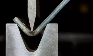 Metalowa blacha jest gięta pod naciskiem stempla, ukazując jeden z rodzajów obróbki plastycznej.