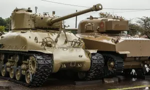 Dwa czołgi Sherman, których kraj pochodzenia to USA, stoją obok siebie na mokrej nawierzchni.