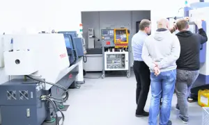 Obrabiarki CNC: co to jest? Grupa mężczyzn ogląda nowoczesne maszyny w hali produkcyjnej.