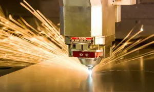 Precyzyjne cięcie metalu przez laser przemysłowy, iskry rozchodzą się na boki.