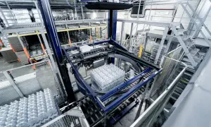 Automatyczne gniazdo produkcyjne pakuje butelki z wodą. Maszyna obraca paletę z napojami, przygotowując ją do dalszego transportu.