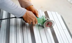 Ręce trzymają szlifierkę kątową, która tnie falistą blachę aluminiową wzdłuż czerwonej linii. To pokazuje, czym ciąć aluminium.