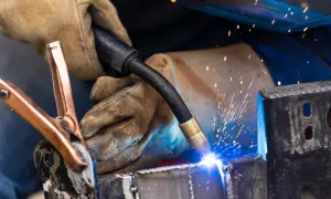 Rękawica ochronna trzyma palnik, z którego wydobywa się jasny łuk elektryczny, tworząc iskry. To proces zimnego spawania metalowych elementów.