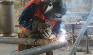 Spawacz w masce i rękawicach łączy metalowe rury. To praca, do której wykorzystuje się spawarkę inwertorową, generującą jasne iskry.