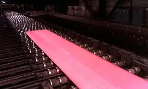 Gorący, różowy metal przesuwa się po rolkach w hucie, będąc częścią cyklu produkcyjnego.