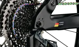 Kolorowy łańcuch rowerowy oplata kasetę zębatek. Widać ramę z napisem "ASSEMBLED IN GERMANY" i flagą. Gwint trójkątny jest kluczowy dla połączeń.