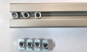 Kilka nakrętek wsuwanych do rowka teowego aluminiowego profilu.