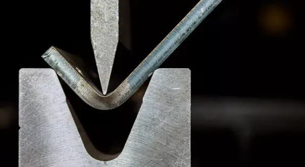 Metalowa blacha jest gięta pod naciskiem stempla, ukazując jeden z rodzajów obróbki plastycznej.