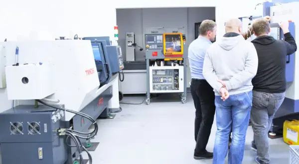 Obrabiarki CNC: co to jest? Grupa mężczyzn ogląda nowoczesne maszyny w hali produkcyjnej.