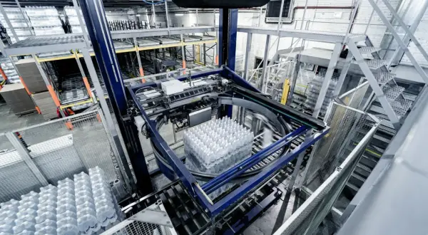 Automatyczne gniazdo produkcyjne pakuje butelki z wodą. Maszyna obraca paletę z napojami, przygotowując ją do dalszego transportu.