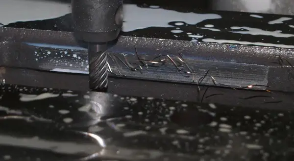 Frezowanie detalu podczas produkcji małoseryjnej. Wióry metalu unoszą się w chłodziwie, tworząc iskry.