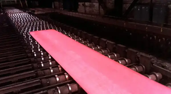 Gorący, różowy metal przesuwa się po rolkach w hucie, będąc częścią cyklu produkcyjnego.