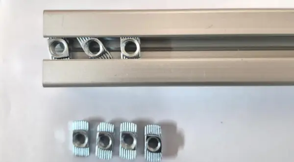 Kilka nakrętek wsuwanych do rowka teowego aluminiowego profilu.