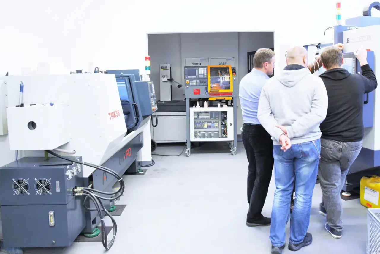 Obrabiarki CNC: co to jest? Grupa mężczyzn ogląda nowoczesne maszyny w hali produkcyjnej.