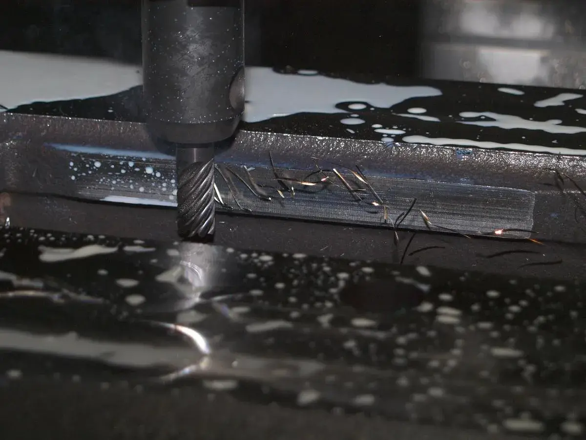Frezowanie detalu podczas produkcji małoseryjnej. Wióry metalu unoszą się w chłodziwie, tworząc iskry.