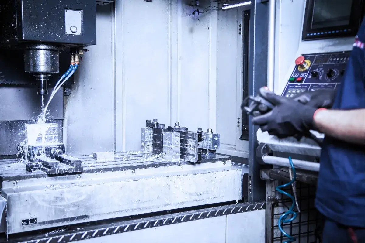 Operator w rękawicach steruje maszyną CNC, która precyzyjnie wykonuje wiercenie otworów w metalowym elemencie, chłodzonym płynem.