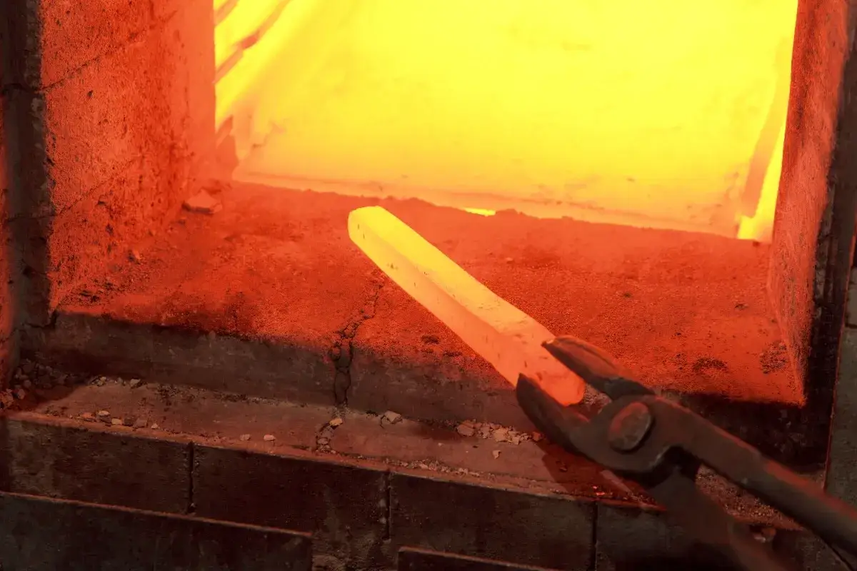 Rozżarzony pręt metalowy, trzymany szczypcami, przechodzi hartowanie na wskroś w rozgrzanym piecu.