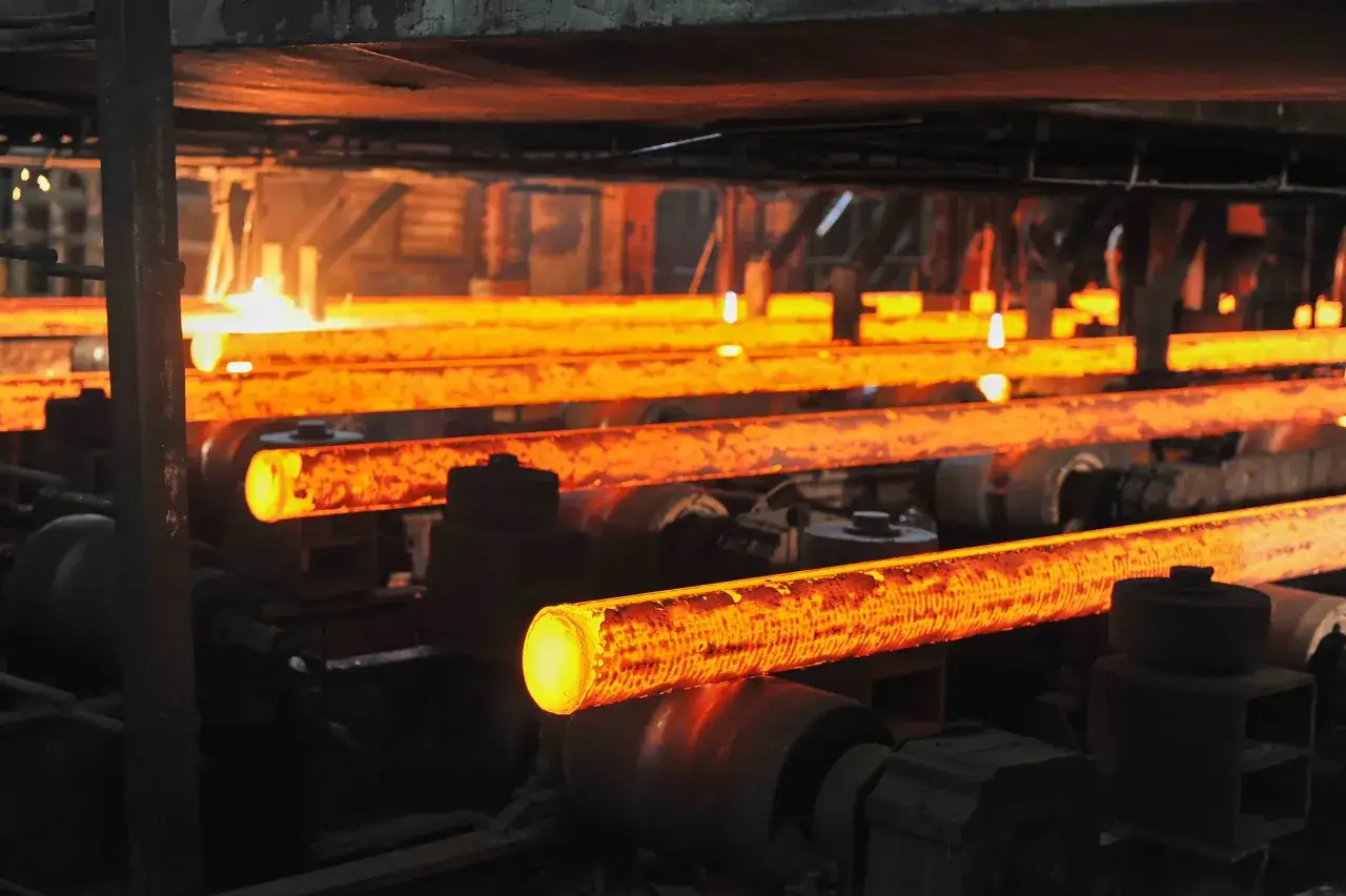 Gorące, żarzące się pręty metalowe, będące materiałami odlewniczymi, przemieszczają się po rolkach w hucie.