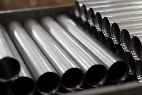 Rury ze stali kwasoodpornej ułożone w pojemniku. Ich gładka, metaliczna powierzchnia odbija światło, tworząc wrażenie czystości i precyzji.