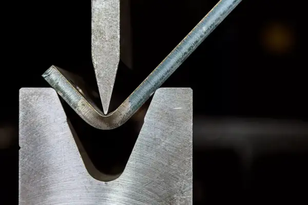 Metalowa blacha jest gięta pod naciskiem stempla, ukazując jeden z rodzajów obróbki plastycznej.