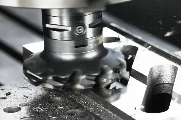 Obrabiarka wykonuje frezowanie czołowe, usuwając materiał z metalowego bloku. Wióry metalu wirują wokół narzędzia.