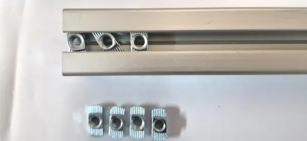 Kilka nakrętek wsuwanych do rowka teowego aluminiowego profilu.